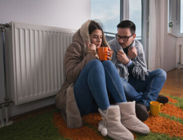 Couple sitting beside radiator and freezing