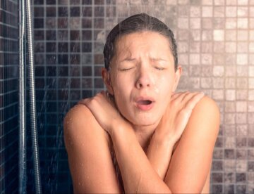 A woman shivers uncontrollably while taking a cold shower.