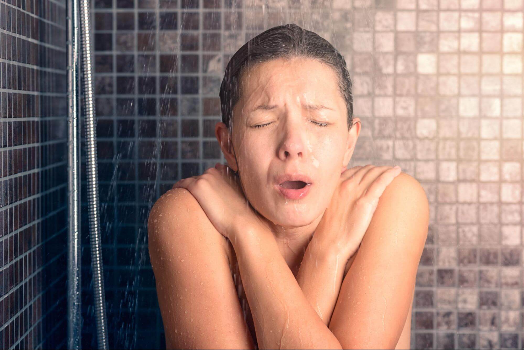 A woman shivers uncontrollably while taking a cold shower.